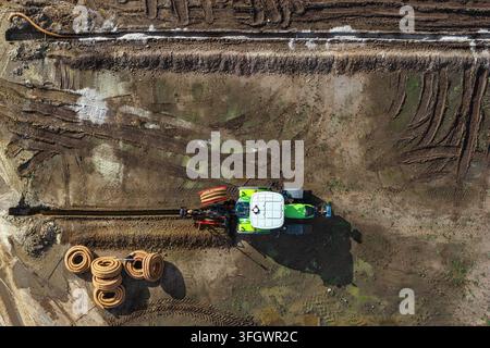 Luftaufnahme eines Traktors, der auf einem schlammigen Feld mit Entwässerungspipelines und Reifenspuren in Enschede, Overijssel, Niederlande arbeitet. Stockfoto
