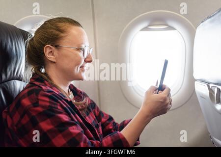 Flugbegleiterin mit Brille nutzt ihr Smartphone im Flugzeug Stockfoto
