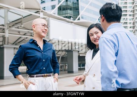 Verschiedenes Geschäftsteam spricht, lacht, fröhliches Gespräch, Modedesignerin, glatzköpfige Frau im Freien. Asiatisches Geschäftsteam trifft sich, Zusammenarbeit mit Partnern Stockfoto