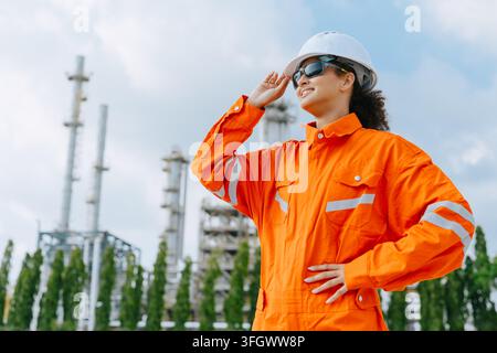 Portrait Erfolg Selbstbewusste Raffinerie-Ingenieurin mit Sicherheitshelm Schutzhelm Außenanlage Industrieanlage Frau Ingenieurin schaut weg selbstbewusst orange Stockfoto