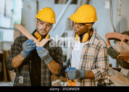 Zwei männliche afrikanische Schwarzarbeiter, Schreiner, die zusammen stehen und eine Holzplatte zur Qualitätskontrolle in einer Möbelwerkstatt inspizieren Stockfoto
