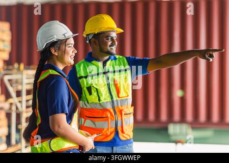 Lagerarbeiter schulen junge Arbeiterin, Hand zeigt lächelnd, trägt Helm und Sicherheitsweste, Versandcontainer-Team. Männlich Weiblich Logistik-Supervisor Stockfoto
