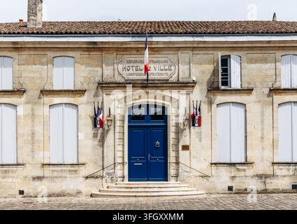 Historisches Rathaus mit französischen Flaggen, Kalksteinfassade und blauer Eingangstür in Saint Emilion, Nouvelle-Aquitaine, Frankreich Stockfoto