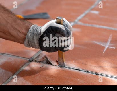 Nahaufnahme einer behandschuhten Arbeiterhand, die ein Meißel hält, während alte Fliesen entfernt werden Stockfoto