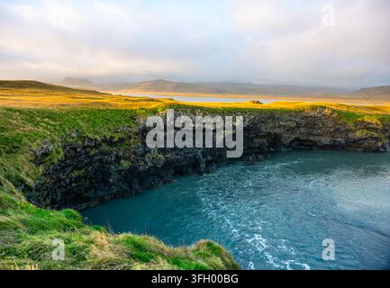 Der Strand von Kirkjufjara bietet schwarzen Sand und einzigartige Felsformationen unter einem pulsierenden Sonnenuntergang. Die Küste bietet sanfte Wellen und malerische Berge Stockfoto
