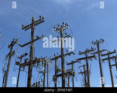 Ansicht von hölzernen Strommasten mit komplexen elektrischen Kabeln und Isolatoren vor einem klaren blauen Himmel in Skiathos, Griechenland. Stockfoto