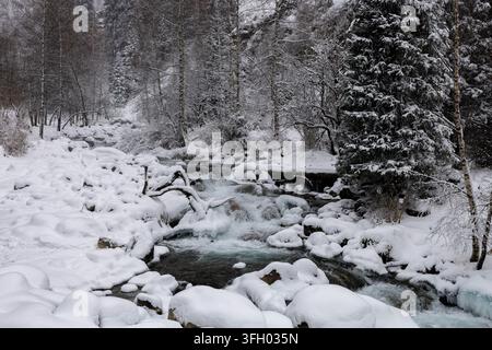 Winterlicher Fluss, der an schneebedeckten Felsen in Kasachstan vorbeifließt Stockfoto