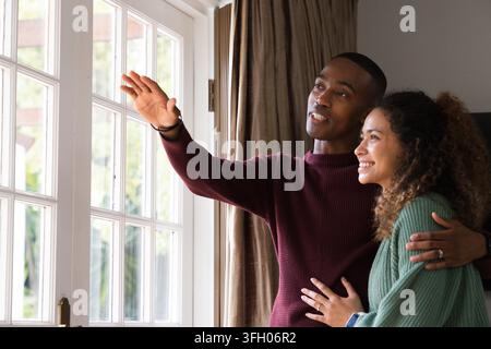 Paar steht neben einer geteilten Glastür zu Hause in der Nähe hoher Vorhänge, Mann zeigt, Ringe sichtbar Stockfoto