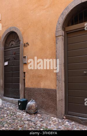 Müllsäcke vor einer alten Holztür auf einer Kopfsteinpflasterstraße, die die Müllabholung in einer historischen Stadt veranschaulicht. Stockfoto