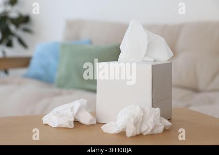 Schachtel Papiertaschentücher und gebrauchte Servietten auf dem Tisch im Innenraum Stockfoto