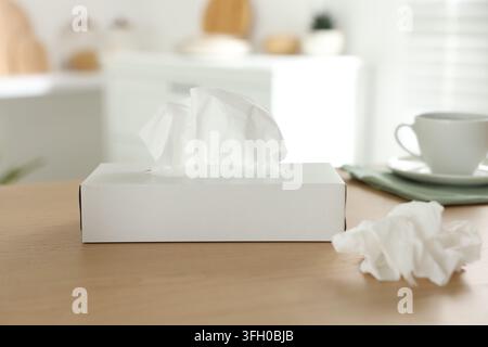 Schachtel mit Papiertaschentüchern und benutzter Serviette auf Holztable im Innenraum Stockfoto