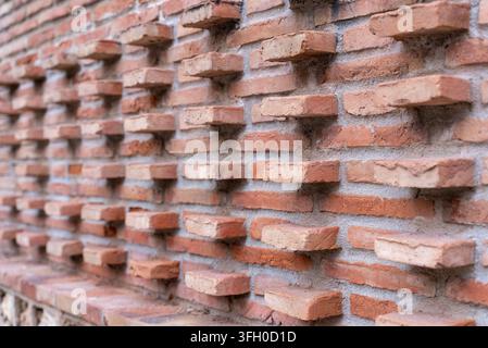 Nahaufnahme einer alten roten Ziegelwand mit unregelmäßig hervorstehenden Ziegeln, die eine strukturierte dekorative Mauerfläche und ein starkes architektonisches Muster erzeugen. Stockfoto