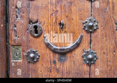 Alte Holztür mit Metallnieten – Nahaufnahme einer rustikalen, verwitterten braunen Holztür, verziert mit antiken dekorativen Metallnieten und einem kunstvollen Schlüssel Stockfoto