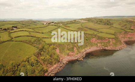 Grüne Felder und Klippen treffen auf das Meer in dieser ländlichen Küstenluftaufnahme, - Drohnenfotografie - Südküste von Devon, England, UK Stockfoto