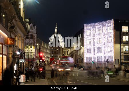 Fußgänger und Verkehr bewegen sich durch Londons Fleet Street vorbei an Weihnachtslichtern, während die St. Paul’s Cathedral im Hintergrund erleuchtet. Stockfoto