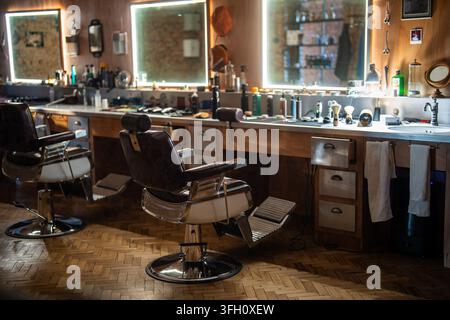 Gemütliches Interieur eines Friseursalons mit klassischen Vintage-Stühlen, beleuchteten Spiegeln und professionellen Werkzeugen. Stockfoto