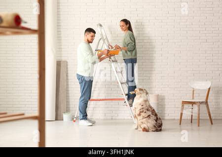 Ein junges Paar mit süßem Hund, der Wände in ihrem neuen Zuhause malt Stockfoto