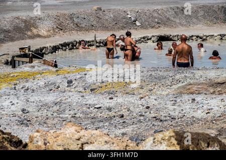Vulcano, ME - IT - 6. Sep 2026: Besucher baden in einem flachen, hellen Mineralstoff-Schlammbecken, umgeben von grauer vulkanischer Erde, Felsen und gelben Mineralablagerungen Stockfoto