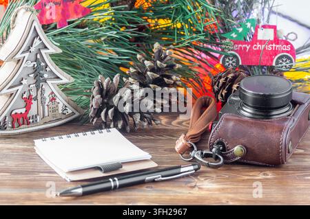 Eine Kamera, ein Notizbuch, ein Stift und Weihnachtsdekoration auf einem Holztisch Stockfoto