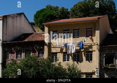 Wäsche trocknet an einer Wäscheleine vor einer gelben Hausfassade mit Ziegeldächern in Guarda, Portugal. Traditionelle Wohnarchitektur und Alltag Stockfoto