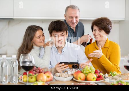 Glückliche Familie, die zusammenhält und auf den Handybildschirm schaut, über lustige Videos oder Fotos in sozialen Netzwerken lacht und zu Hause Spaß hat Stockfoto
