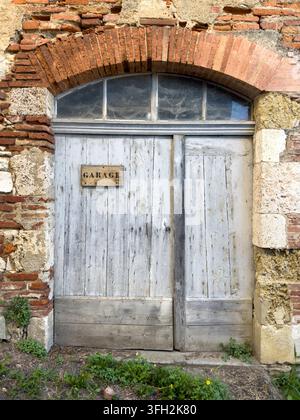 Verwitterte hölzerne Garagentür in einem runden Ziegelbogen, Gers, Gimont, Frankreich Stockfoto