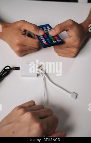 Vertikal beschnittener Shot von zwei Technikern, die RGB-LED-Streifen verbinden und einen kabellosen Controller für personalisierte Umgebungsbeleuchtung in modernen Räumen konfigurieren Stockfoto