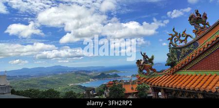 Ein atemberaubender Panoramablick von einem verzierten chinesischen Tempeldach mit detaillierten Drachen-Schnitzereien und orangefarbenen Ziegeln, der über üppige grüne Berge blickt. Stockfoto