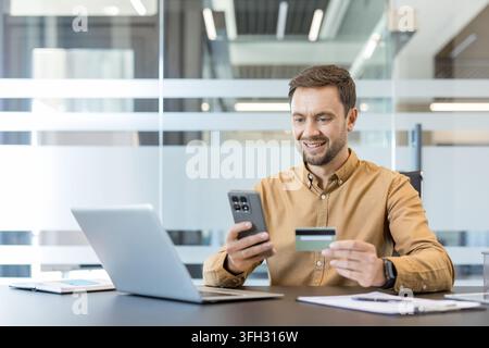 Online-Shopping und digitale Zahlung, Mann verwendet Smartphone und Kreditkarte für E-Commerce-Transaktion am Bürotisch. Sichere Finanztechnologie und mobiles Banking. Stockfoto