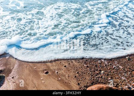 Meereswelle mit weißem Schaum, die über einen kiesigen Sandstrand schwappt. Stockfoto