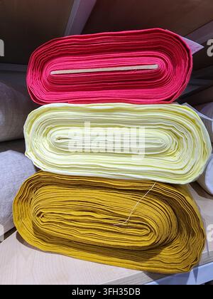 Verschiedene Stoffschrauben mit verschiedenen Texturen und Farben, die auf einem Holzregal angeordnet sind, veranschaulichen Materialoptionen zum Nähen, Basteln und Desi Stockfoto
