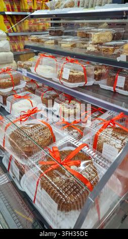 Verschiedene verpackte Kuchen und Gebäck mit roten Bändern, die in Regalen in der Bäckereiabteilung eines Lebensmittelladens oder Supermarkts liegen und ein schnelles Dessert bieten Stockfoto