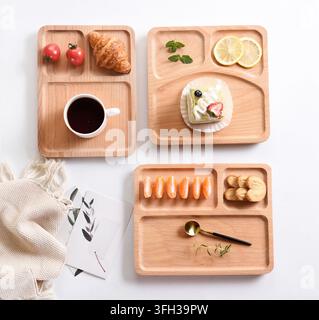 Leichte hölzerne, unterteilte Tabletts gefüllt mit verschiedenen Frühstücksgebäck, Kaffee und frischen Früchten auf weißem Hintergrund Stockfoto