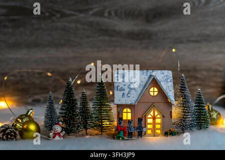 Miniaturhaus beleuchtet eine festliche Winterszene mit Bäumen und Schnee Stockfoto