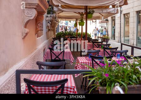 Außenterrasse eines italienischen Restaurants mit roten karierten Tischdecken und Sonnenschirmen in Verona, Italien. Stockfoto