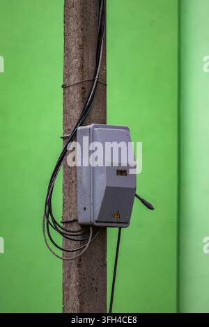 Ein grauer Elektrikschrank mit einem Hochspannungssymbol ist an einem Betonmast mit freiliegenden Drähten angebracht. Der Mast steht vor einem vibrierenden Stockfoto