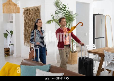 Paar trägt schwarze Koffer und gelben Regenschirm, hält braune Handtasche in heller Wohnung Stockfoto
