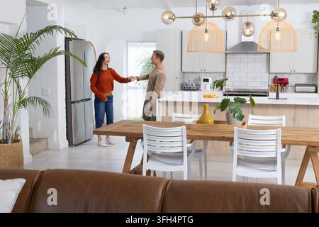 Paar, das Schlüssel übergibt, während es in der Küche in der Nähe einer Insel mit rotem Kaffeekocher und Holztisch steht Stockfoto