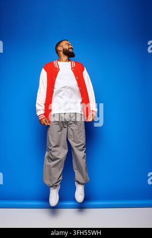 Ein junger, gutaussehender Mann springt und präsentiert sein stylisches Outfit und sein strahlendes Lächeln. Stockfoto