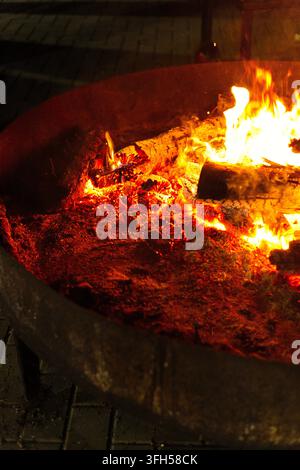 Feuer, das in einem Metallkamin mit dunklem Hintergrund brennt. Glühende Kohlen leuchten mit hoher Temperatur. Stockfoto