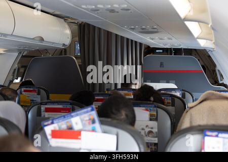 Passagiere, die während des Fluges in der Kabine eines Verkehrsflugzeugs sitzen, mit Sitzreihen, Gepäckfächern über den Sitzen und dem vorderen Teil des Flugzeugs Stockfoto
