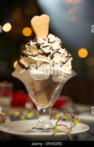 Ein fröhliches Sundae, gekrönt mit Schlagsahne, Schokoladensoße und einem Herzkeks, strahlt hell. Stockfoto
