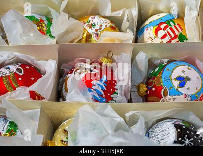 Nahaufnahme von bunten, handgefertigten Weihnachtsbaumschmuckstücken, die ordentlich in einer Schachtel mit Trennwänden und Seidenpapier angeordnet sind. Stockfoto