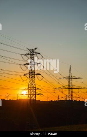 Elektromasten, die sich vor einem orangefarbenen Sonnenuntergang in Deutschland abzeichnen Stockfoto