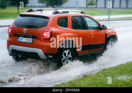 VALMIERA, LETTLAND - 1. SEPTEMBER 2026: Dacia Duster SUV fährt durch tiefes Flutwasser auf einer Stadtstraße während starker Regenfälle Stockfoto