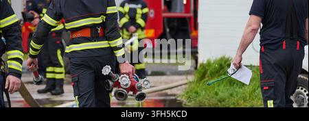 Feuerwehrmänner arbeiten zusammen und tragen Schläuche und Hydrantenverteiler in der Nähe des Feuerwehrautos während der Notfallreaktion Stockfoto