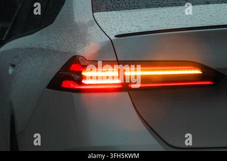 Nahaufnahme des beleuchteten hinteren LED-Rücklichts und des Blinkers an einem nassen modernen Auto bei starkem Regen Stockfoto