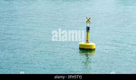 Eine gelbe Solar-Navigationsboje schwimmt auf blauem Wasser mit ihrer Spiegelung. Konzept von Navigation, Sicherheit, Transit, Ausrüstung und mariner Infrastruktur Stockfoto