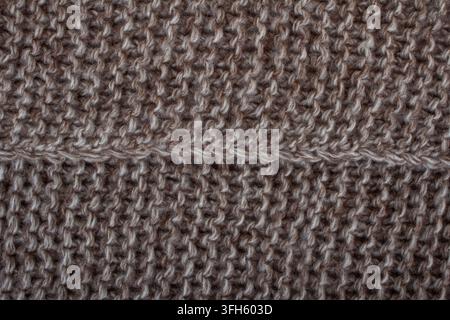 Nahaufnahme der Textur von braunem und beigem gestricktem Wollstoff mit deutlicher Nahtlinie in der Mitte. Rustikaler warmer Strickpullover-Hintergrund. Stockfoto