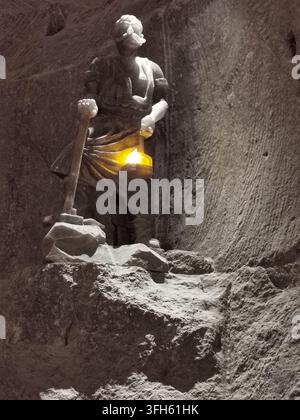 WIELICZKA, POLEN – 16. SEPTEMBER 2022: Eine aus Salz gehauene Statue eines Bergmanns, der eine Hacke und eine leuchtende Laterne hält, steht in einer dunklen Kammer Stockfoto